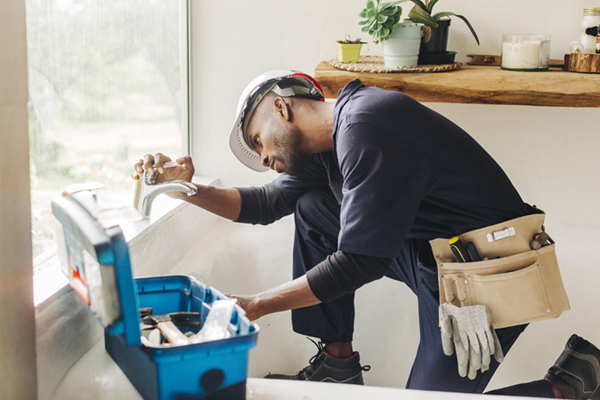 Plumber fixing a faucet in a home bathroom with a toolbox beside him.