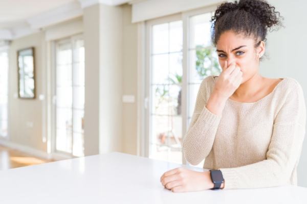 Woman covering her nose due to a musty smell in her home caused by water damage.