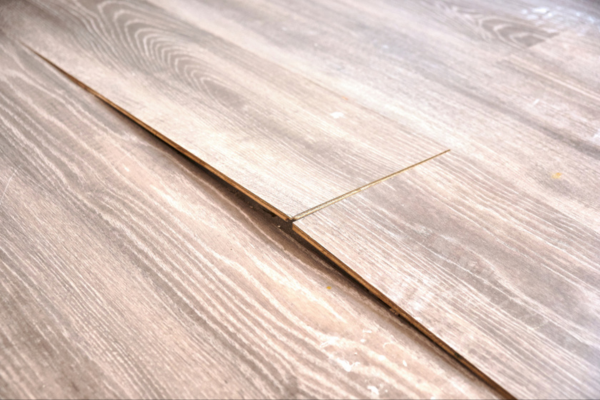 Close-up of laminate flooring with buckling and uneven seams caused by water damage.