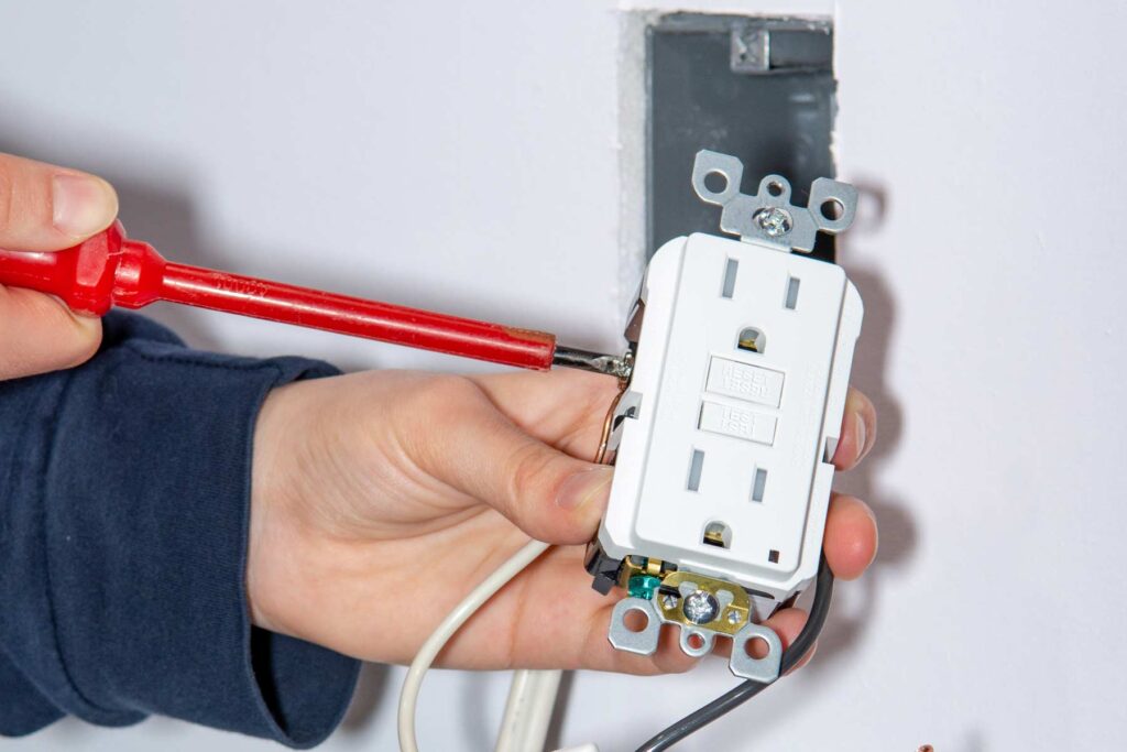 A person installing a GFCI outlet with a screwdriver.