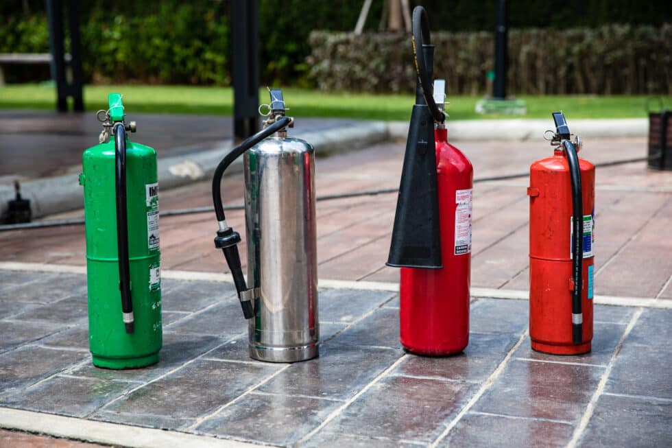 Different types of fire extinguishers lined up outdoors.