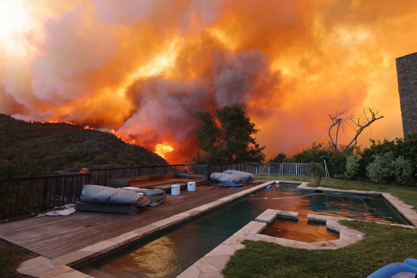 A serene backyard with a pool, set against a backdrop of massive wildfires in the hills.