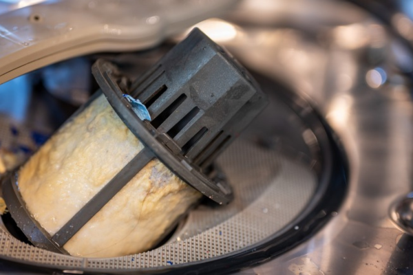 Clogged dishwasher drain with food particles causing water overflow.